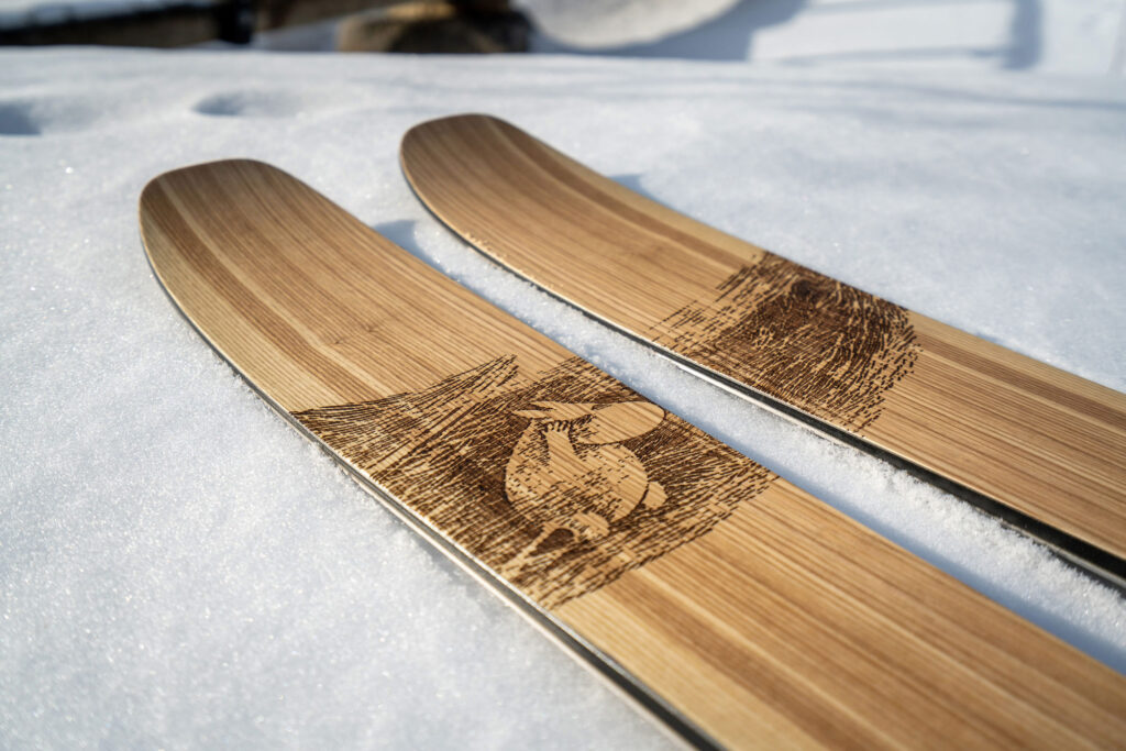 Drewniane narty skiturowe PUSU x Moomin – model Abisko z grafiką Muminka przedzierającego się przez zamieć śnieżną.